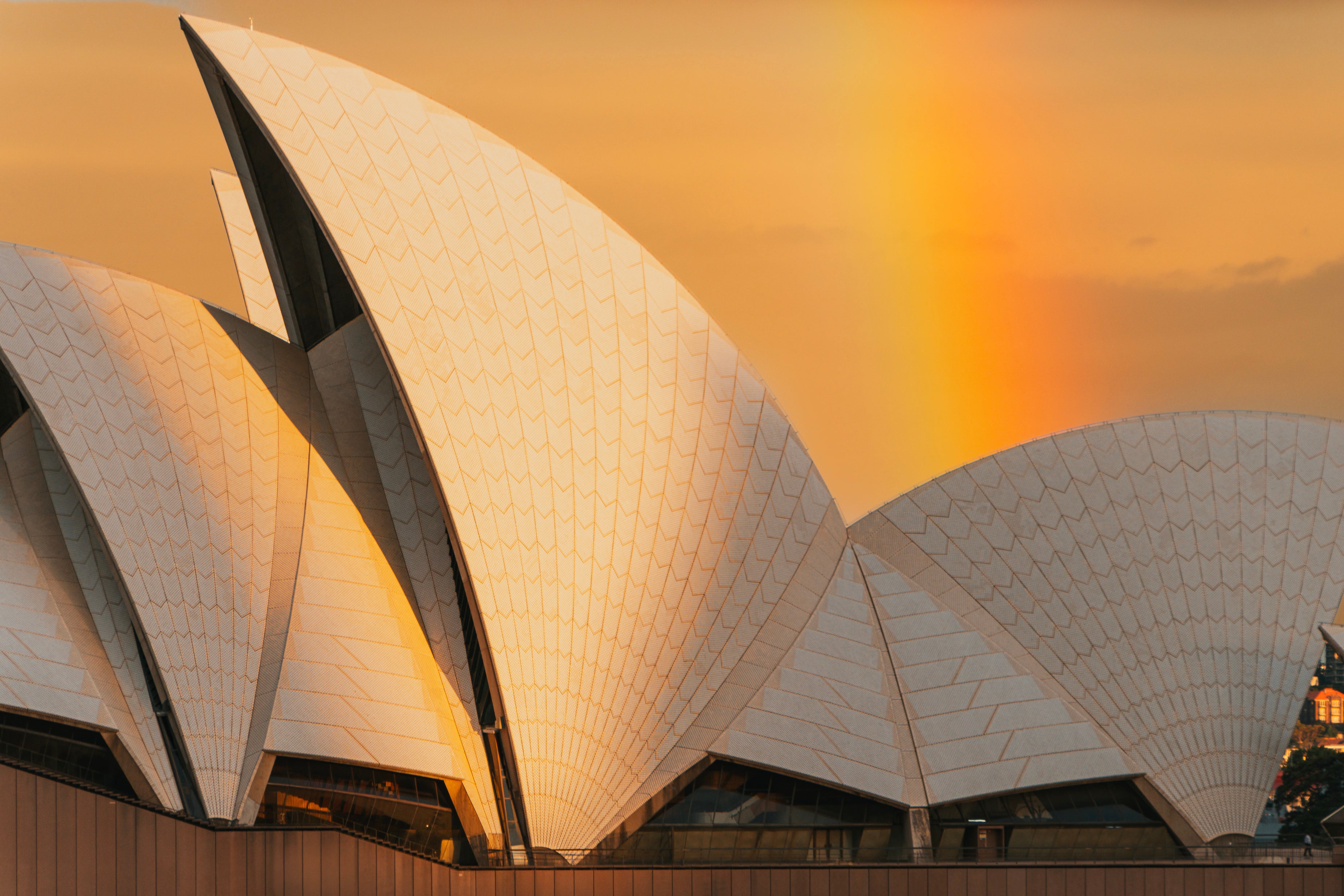 The Sydney Opera House sails lit by a warm sunset with a rainbow arcing behind.