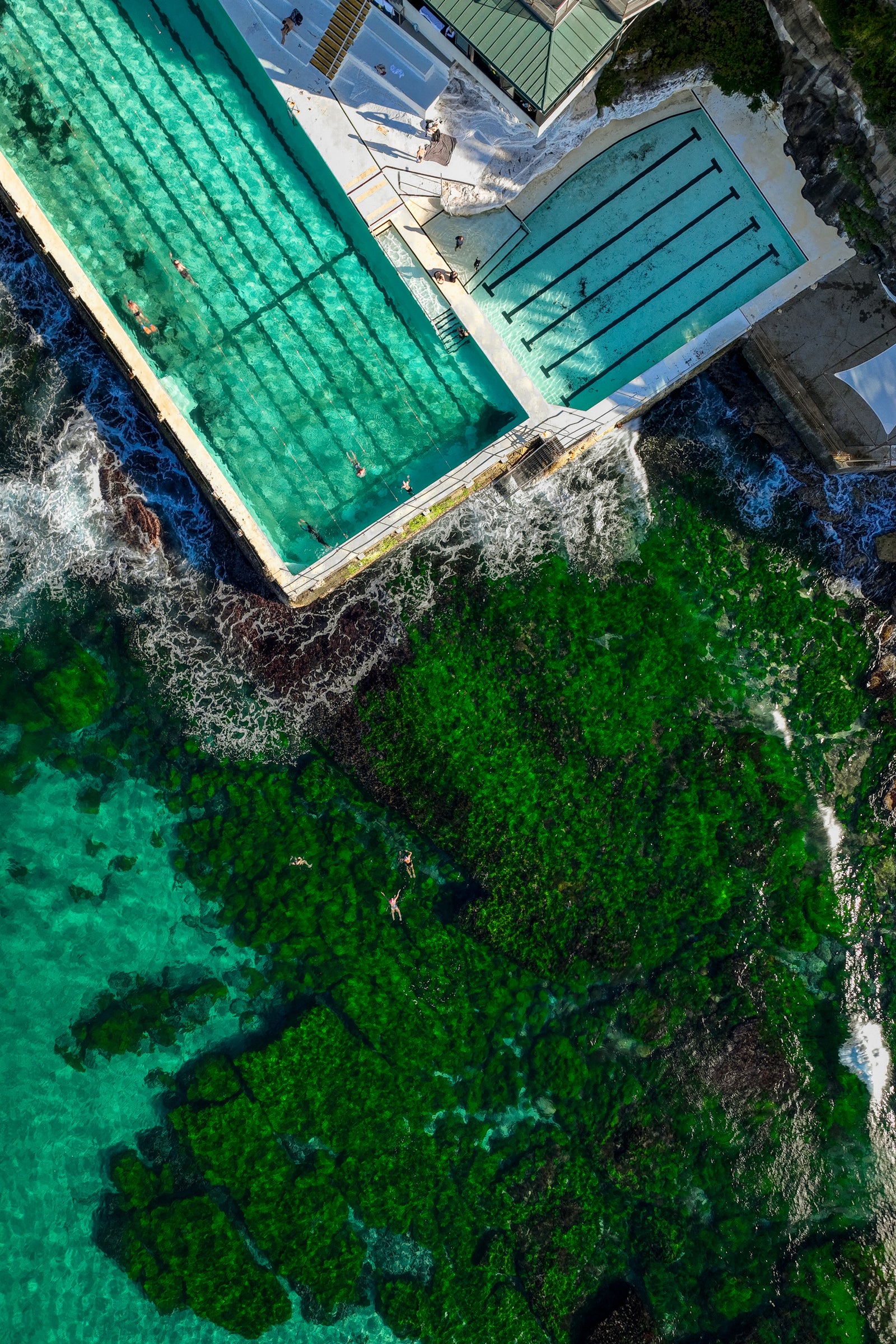 An aerial top-down view of the Bondi Icebergs ocean pool in Australia with swimmers and waves crashing against the concrete pool edge.