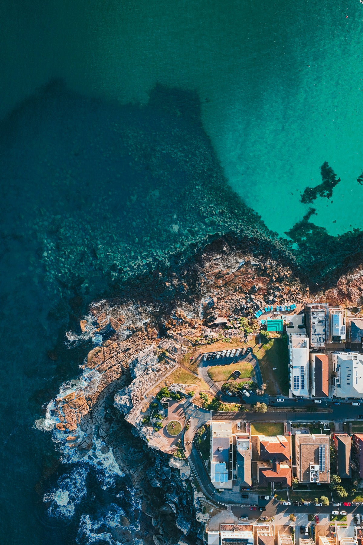 An aerial top-down view of the rocky North Bondi coastline meeting the deep blue and turquoise Pacific Ocean.