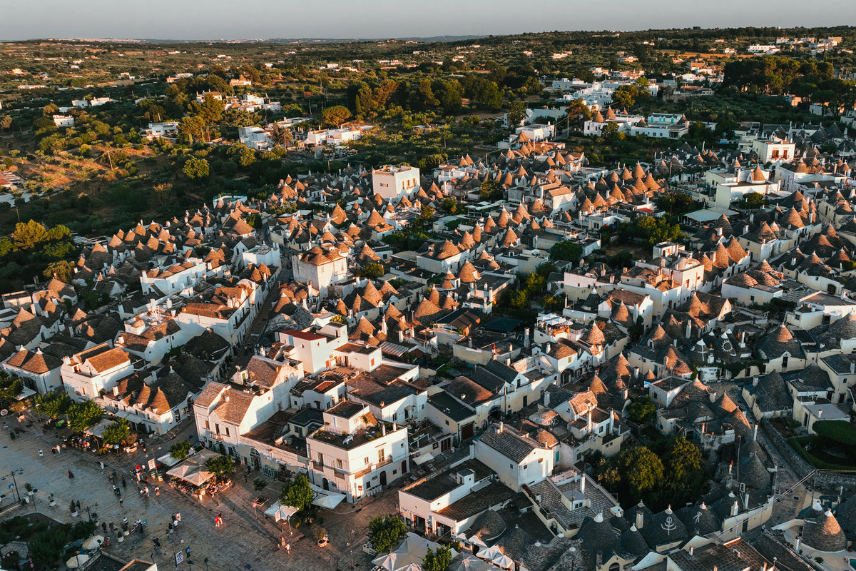 Aerial photograph at golden hour capturing the clusters of traditional cone-shaped trulli rooftops in Alberobello, Italy.
