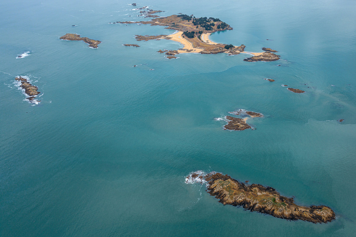 High-angle aerial view of rocky islands with small sandy beaches surrounded by turquoise ocean water in Brittany, France.