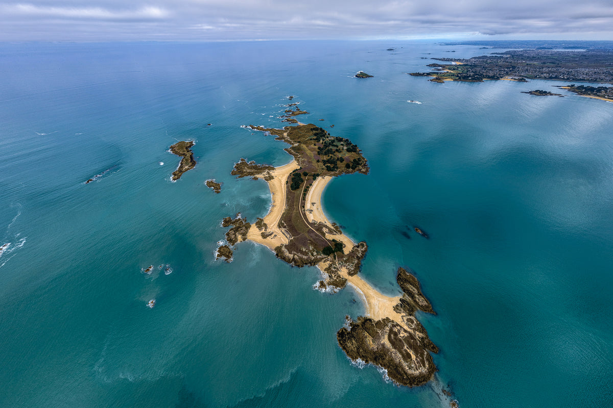 High angle aerial view of a rugged green island surrounded by turquoise sea water in France.