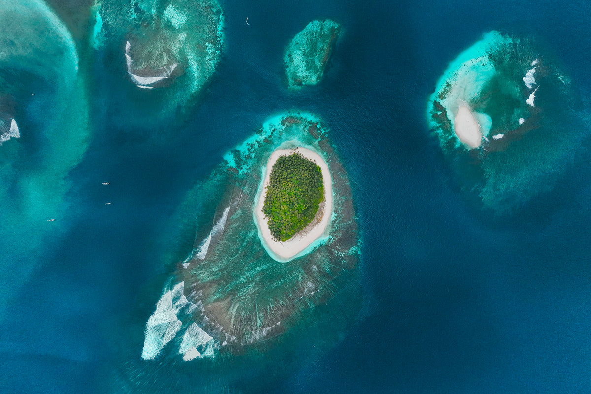An aerial top-down view of small tropical islands with white sand and palm trees surrounded by coral reefs in Panama.