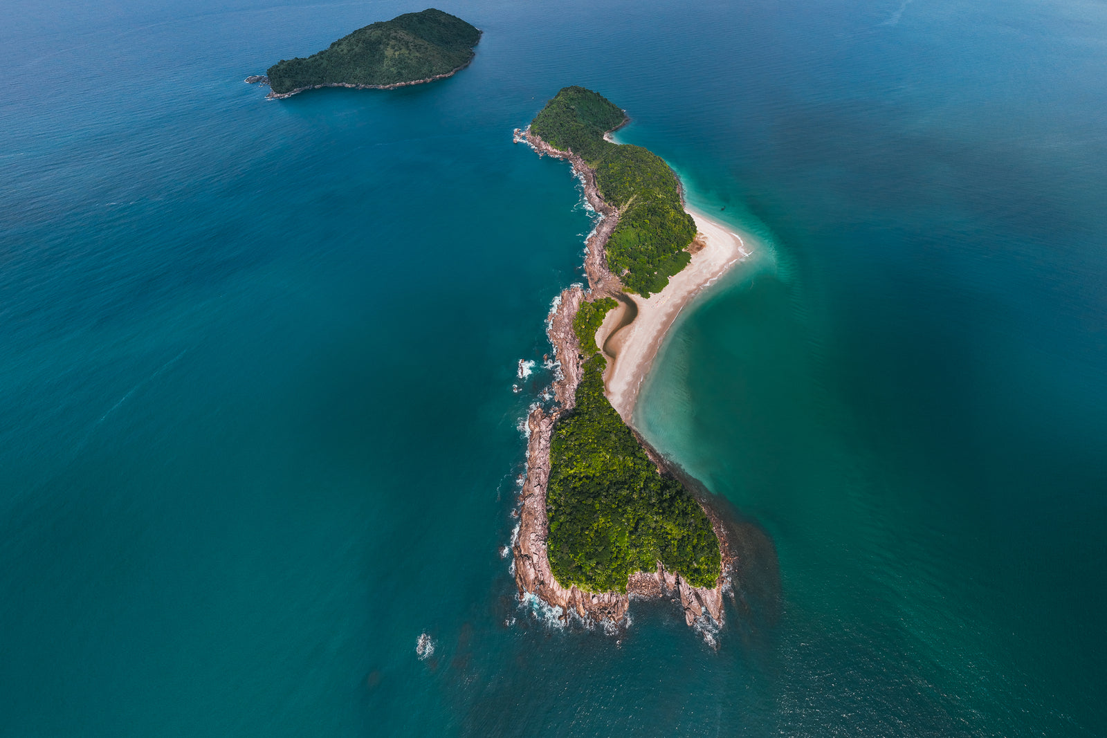 An aerial photograph of a lush green island with a white sandy beach in the middle of a vast turquoise and deep blue ocean.