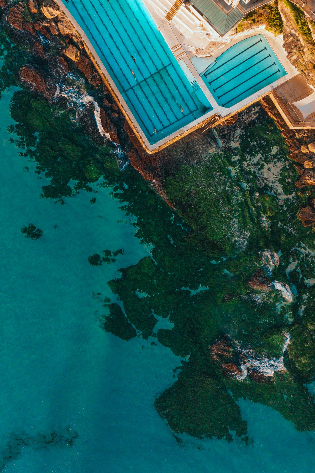 An aerial top-down view of the Bondi Icebergs ocean pool next to mossy green rocks and turquoise water in Australia.