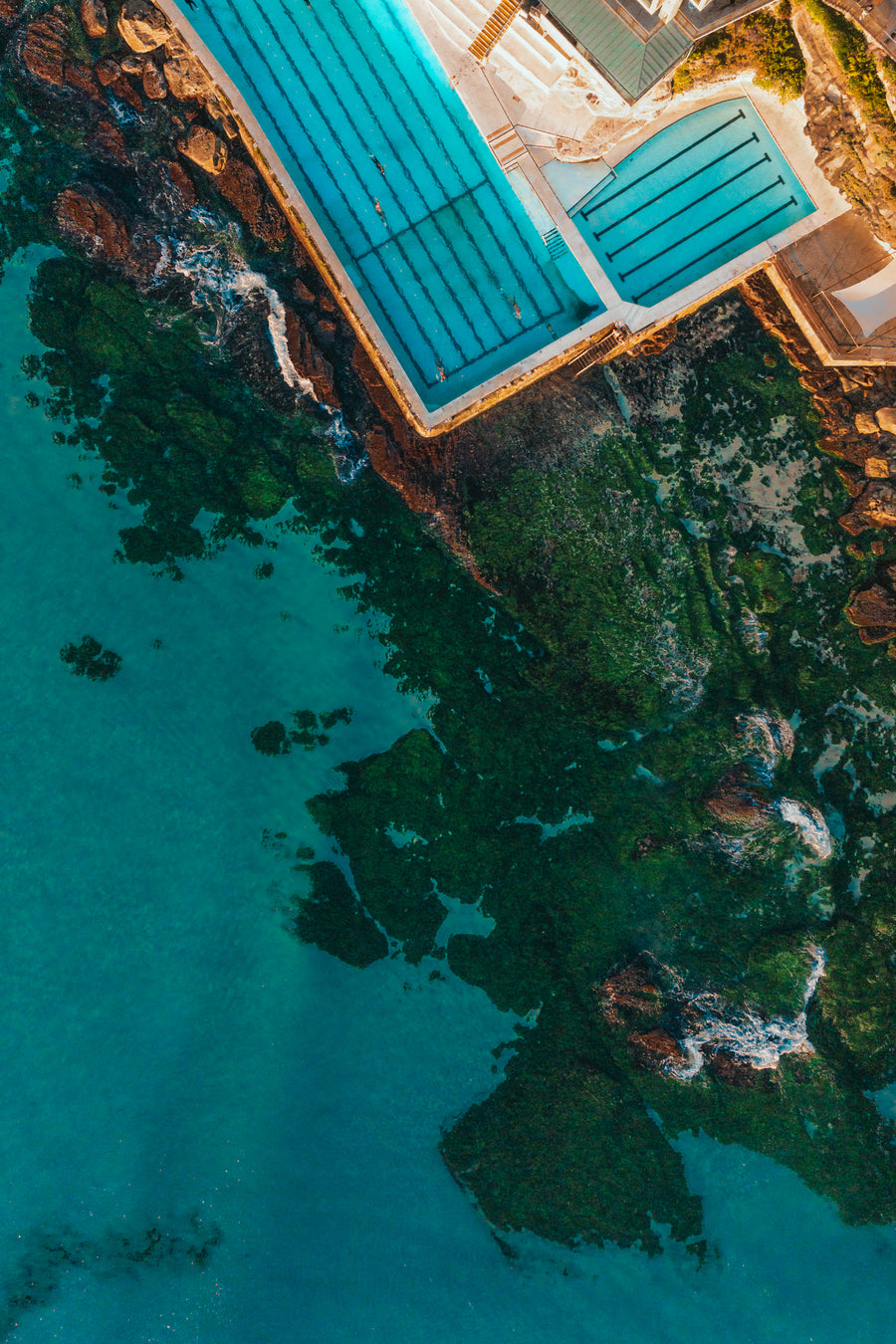 An aerial top-down view of the Bondi Icebergs ocean pool next to mossy green rocks and turquoise water in Australia.