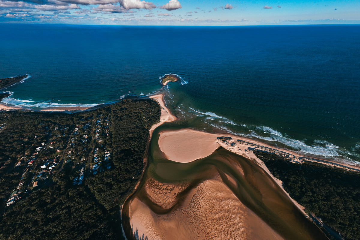 An aerial view of the Crescent Head estuary in Australia, showing the meeting point of the river, sandy dunes, and the blue ocean.